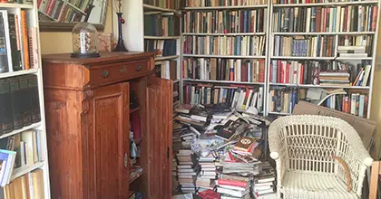 Zimmer mit vollgestellter Bücherwand und unsortiertem Bücherstapel davor